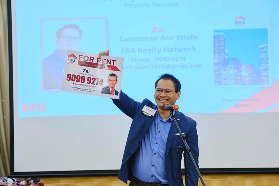 Zai presenting on stage with the ERA Realty Network FOR RENT sign